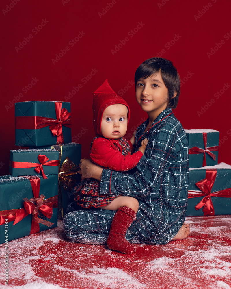 brother and sister are sitting on the floor among green New Year gift boxes on a red background with snow.