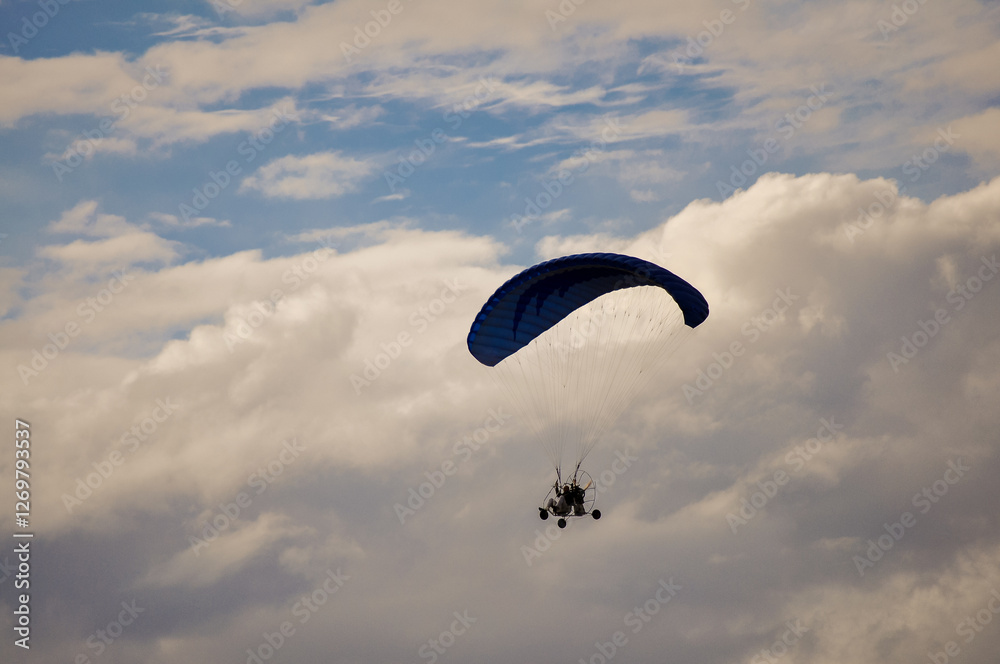 A paraglider flies through the sky above the mountains, carried by the wind. The paraglider is a bright orange color, and the pilot is silhouetted against the sky. The mountains are green and lush, an A paraglider flies through the sky above the mountains, carried by the wind. The paraglider is a bright orange color, and the pilot is silhouetted against the sky. The mountains are green and lush, an