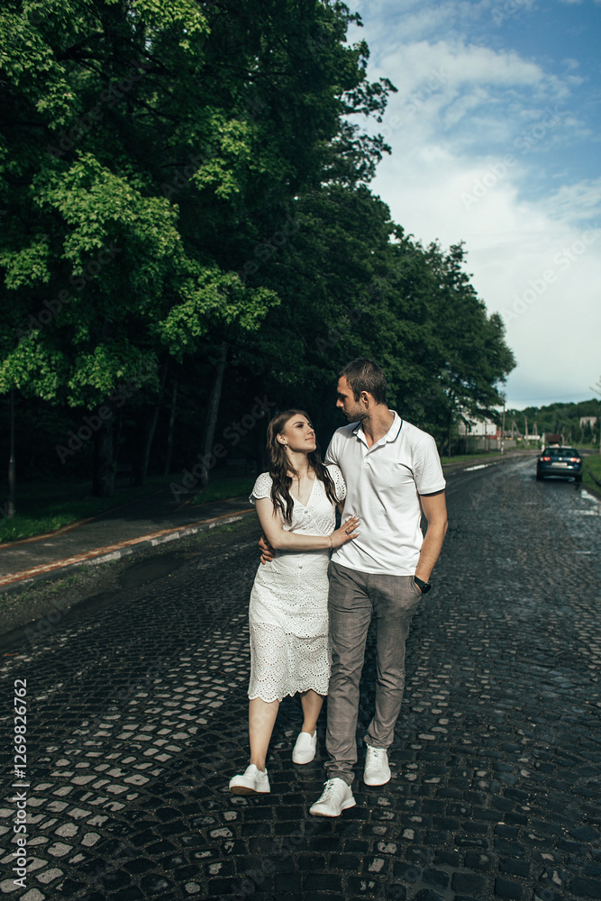 a man and a woman hug each other and look at each other. Green trees and a parked car are visible in the background. a man and a woman hug each other and look at each other. Green trees and a parked car are visible in the background.