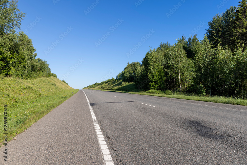 an empty straight paved road against a blue sky background an empty straight paved road against a blue sky background