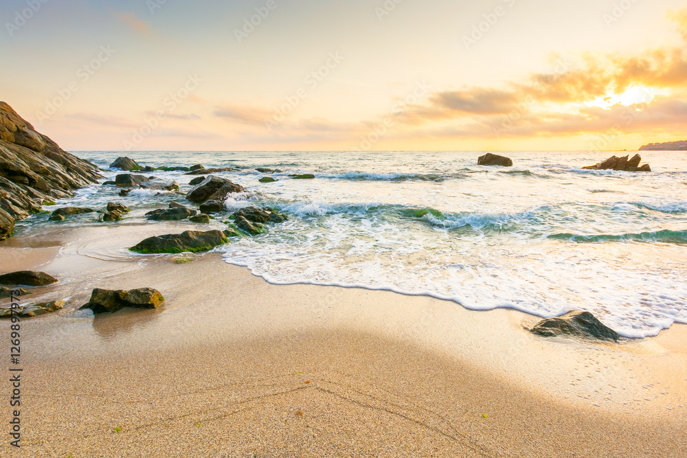 summer holiday season at the seaside. beautiful seascape at sunrise. golden sandy beach in morning light. sun behind fluffy clouds on sky above horizon. scenic travel background with rocks and waves