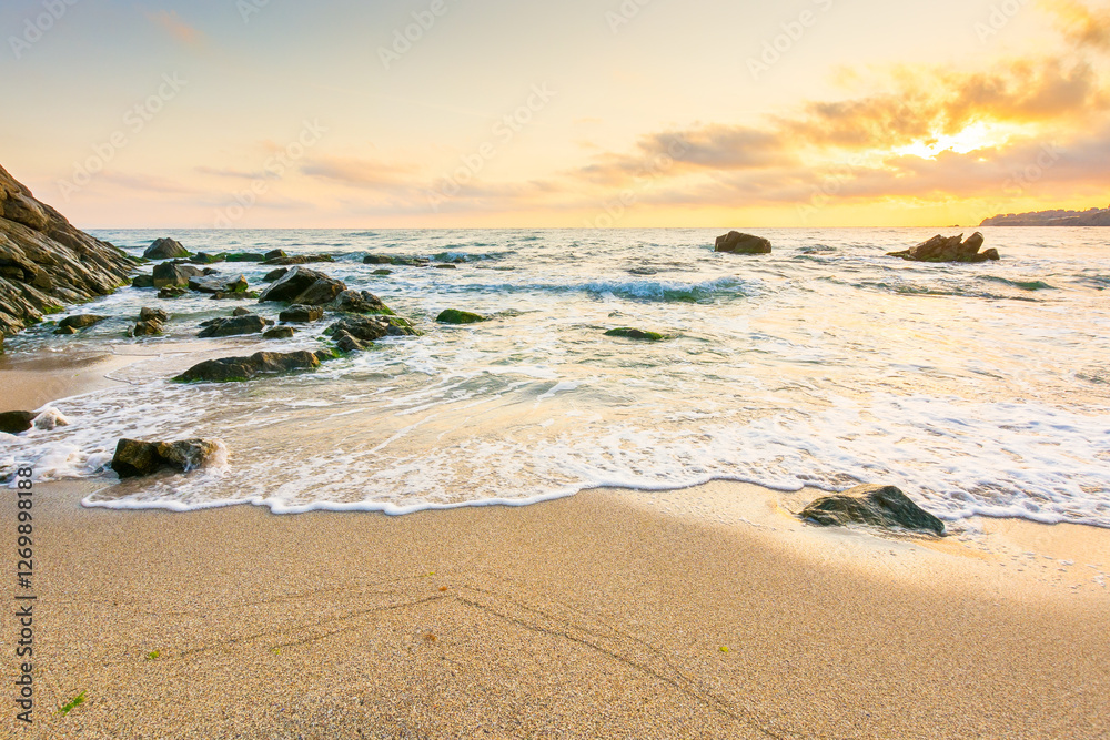 summer holiday season at the seaside. beautiful seascape at sunrise. golden sandy beach in morning light. sun behind fluffy clouds on sky above horizon. scenic travel background with rocks and waves