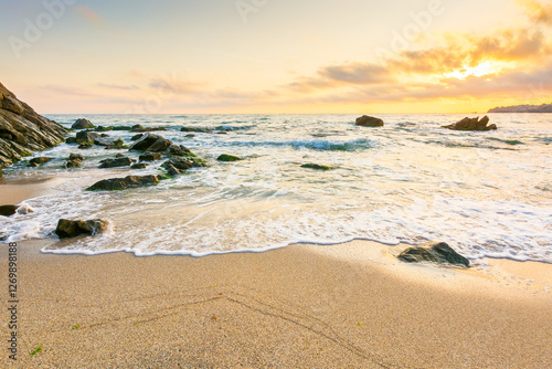 summer holiday season at the seaside. beautiful seascape at sunrise. golden sandy beach in morning light. sun behind fluffy clouds on sky above horizon. scenic travel background with rocks and waves