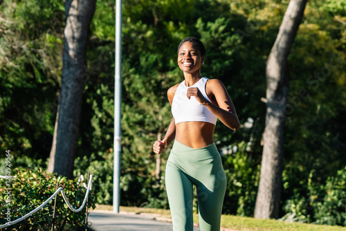 Young sporty black woman running in a green park