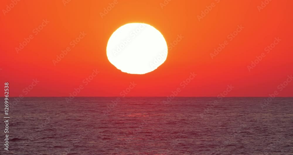 Ultra zoom on big bright disc of sun on red sky reflecting in the sea waves at sunset