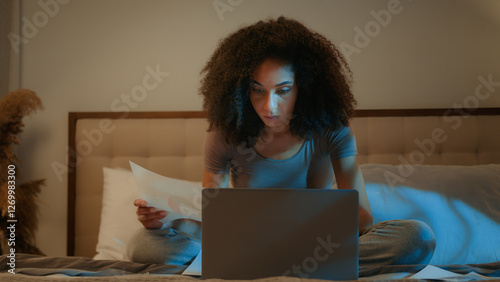 African American woman businesswoman working from home paperwork laptop computer overtime night late work check domestic utility bills female student girl prepare to exam studying in evening on bed