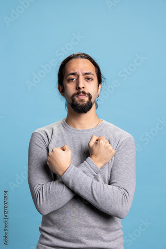 Self assured young guy standing with his arms crossed on his chest in studio, acting determined and showing his strength. Serious person with a cool vibe focused on empowerment against background.