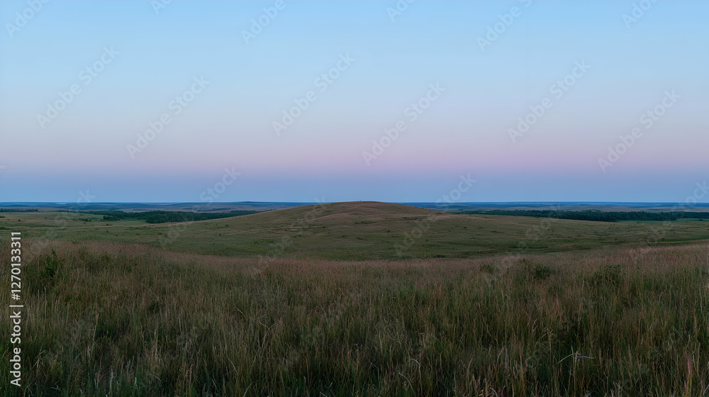 Fototapeta premium Rolling green hills of a vast prairie landscape under a soft pink and blue twilight sky at dusk.