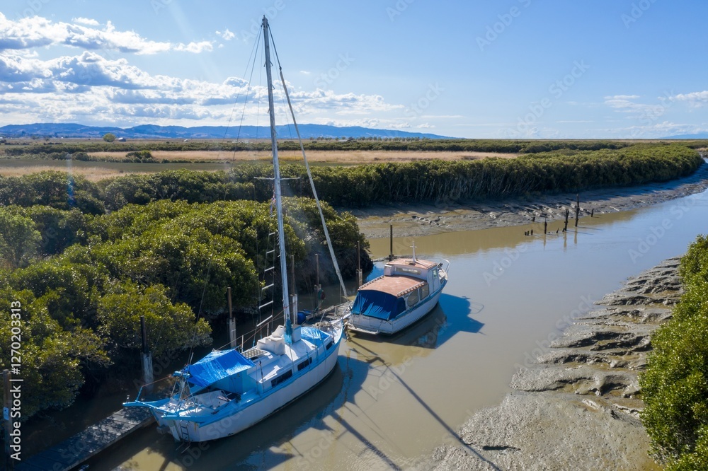 Two boats moored at low tide in a sheltered estuary. Tranquil scene of calm water and lush vegetation. Waitakaruru, Thames, Waikato Region, New Zealand Two boats moored at low tide in a sheltered estuary. Tranquil scene of calm water and lush vegetation. Waitakaruru, Thames, Waikato Region, New Zealand