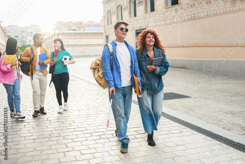 Happy blind man walks with group of friends inside school or university campus. People students, education concept