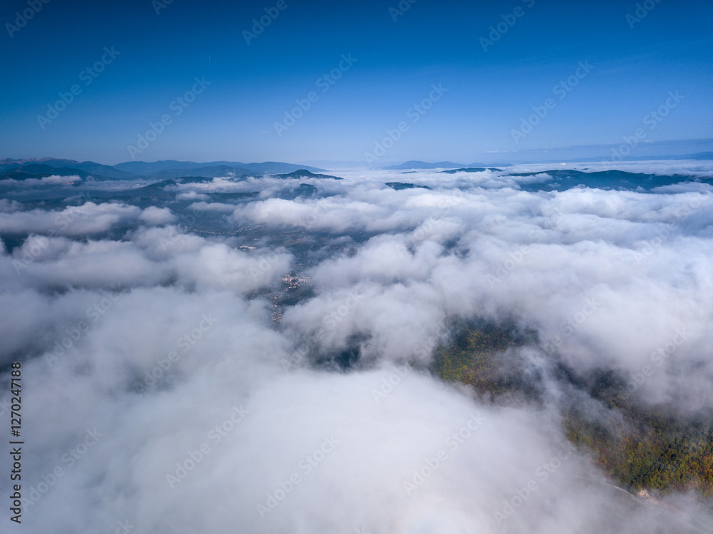 Aerial view of fluffy clouds blanketing a landscape with blue sky and distant mountain ranges Aerial view of fluffy clouds blanketing a landscape with blue sky and distant mountain ranges