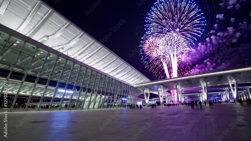 Wide-angle video capturing a modern building with glass facade at night, featuring vibrant fireworks illuminating the sky above.
