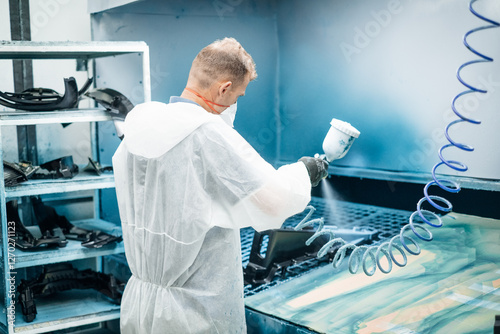 Protective gear worker using spray gun in a painting booth Automotive part manufacturing process