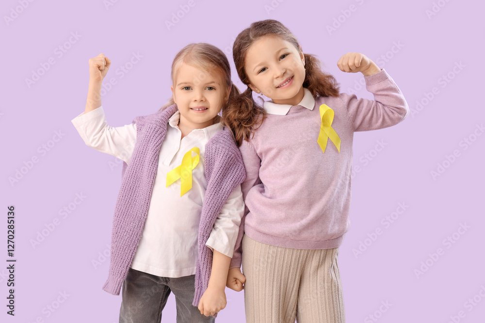 Cute little girls with yellow ribbons showing muscles on lilac background. Childhood cancer awareness concept Cute little girls with yellow ribbons showing muscles on lilac background. Childhood cancer awareness concept