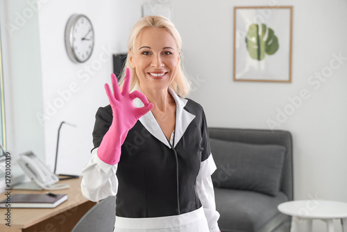 Middle-aged chambermaid showing OK in hotel room