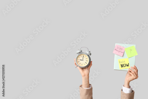 Woman holding alarm clock with notebook on grey background. Time management concept