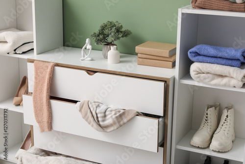Shelving units with commode and scattered clothes near green wall in messy living room, closeup