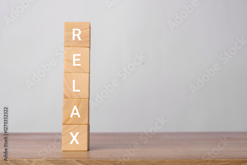 Relax word written vertically on wooden blocks on a wooden table with a light gray background. Calm and stress relief concept