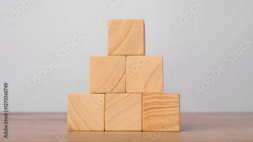 Wooden blocks stacked in a pyramid shape on a wooden table with a light gray background. Structure and stability concept