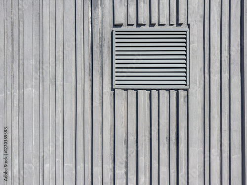 metal lattice of a technical window of ventilation on a gray ridge concrete wall.