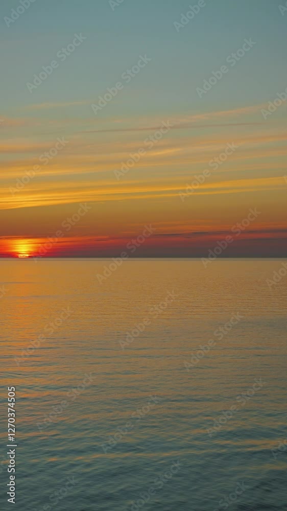 A serene sunset over calm waters where bright orange and yellow hues blend with a peaceful blue sky. The sun is halfway over the horizon A serene sunset over calm waters where bright orange and yellow hues blend with a peaceful blue sky. The sun is halfway over the horizon