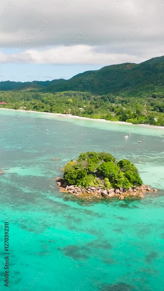 A vibrant island nestled in turquoise waters, featuring lush greenery and rocky shores. Praslin, Seychelles.