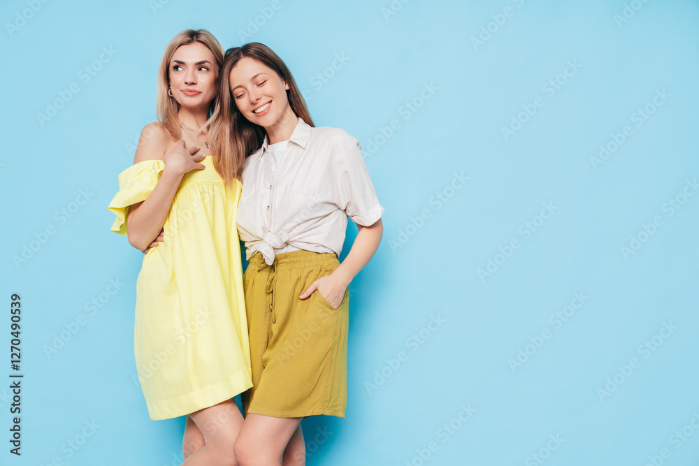 Two young beautiful smiling brunette and blond hipster female in trendy summer clothes. Lovely women posing on blue background in studio. Positive models having fun. Cheerful and happy. isolated Two young beautiful smiling brunette and blond hipster female in trendy summer clothes. Lovely women posing on blue background in studio. Positive models having fun. Cheerful and happy. isolated