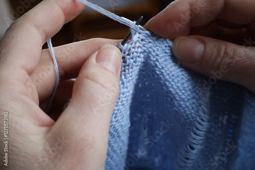 Women's hands are knitting purl loops with blue yarn. Close-up.