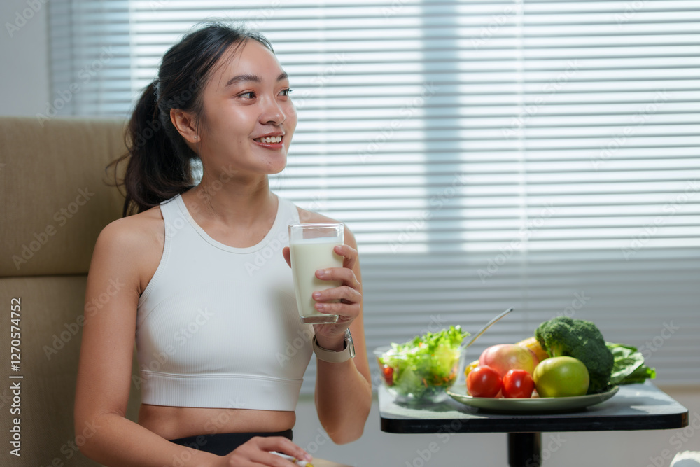 Smiling sportswoman drinking milk, with a plate of fresh fruits and vegetables on the table, promoting a healthy lifestyle and balanced diet Smiling sportswoman drinking milk, with a plate of fresh fruits and vegetables on the table, promoting a healthy lifestyle and balanced diet