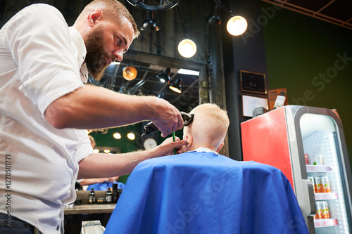 Barber using comb and shaver to cut hair. Professional hairdresser shaving little kid's nape.