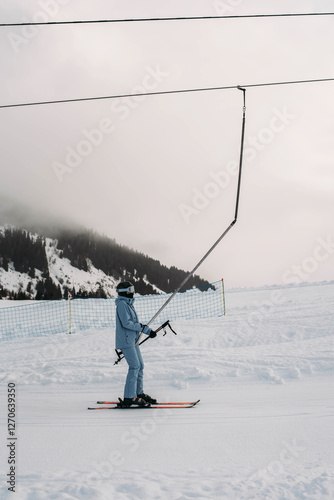 Young woman in blue ski suit climbs uphill on platter lift photo