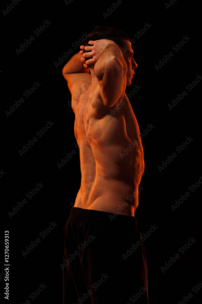 Fototapeta premium Adult male athlete bodybuilder posing on a orange light