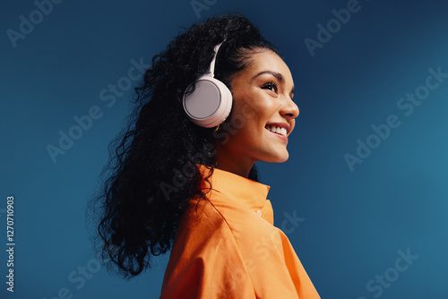Woman wearing headphones in a vibrant orange and blue monochromatic studio setting, smiling and enjoying music