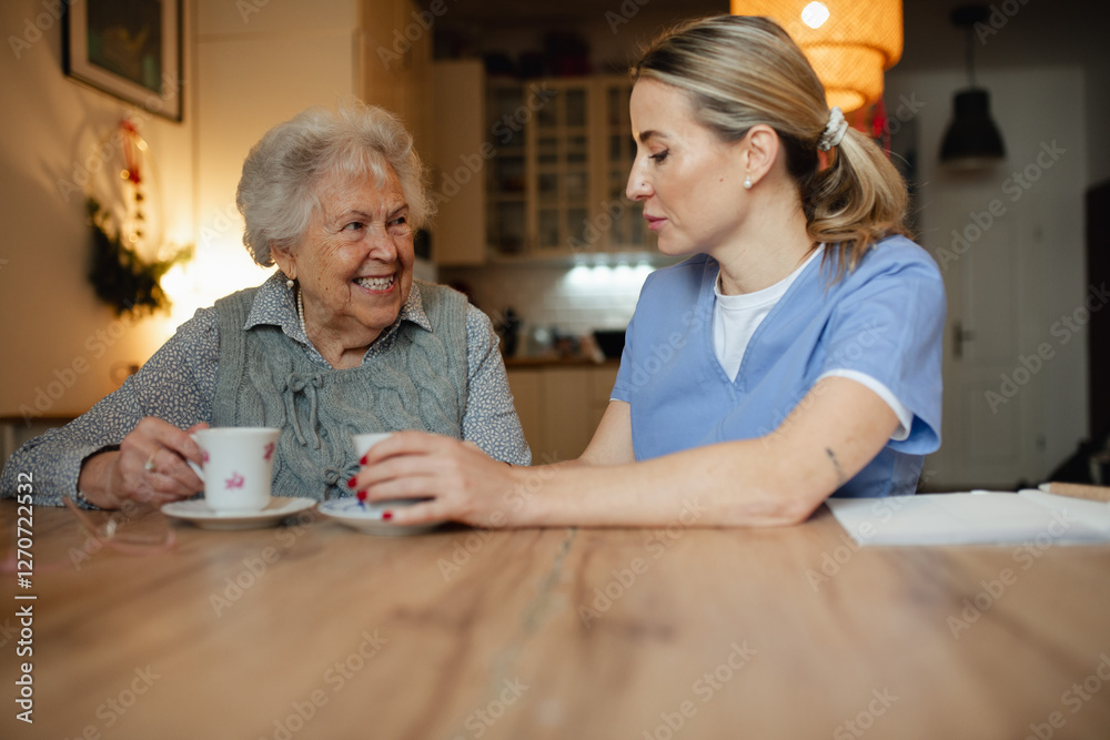 Obraz premium Lovely eldery woman serving tea to friendly caregiver during home visit.