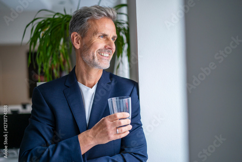 Happy businessman with glass of water standing at office