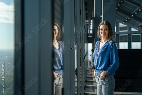 Smiling businesswoman standing with hands in pockets near window at office photo