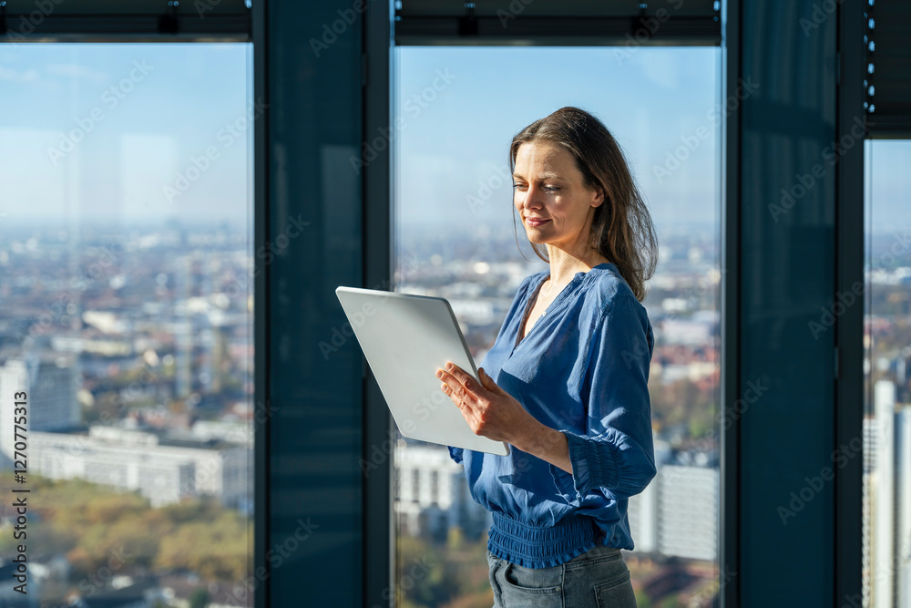 Smiling mature businesswoman using tablet PC in front of window at office Smiling mature businesswoman using tablet PC in front of window at office
