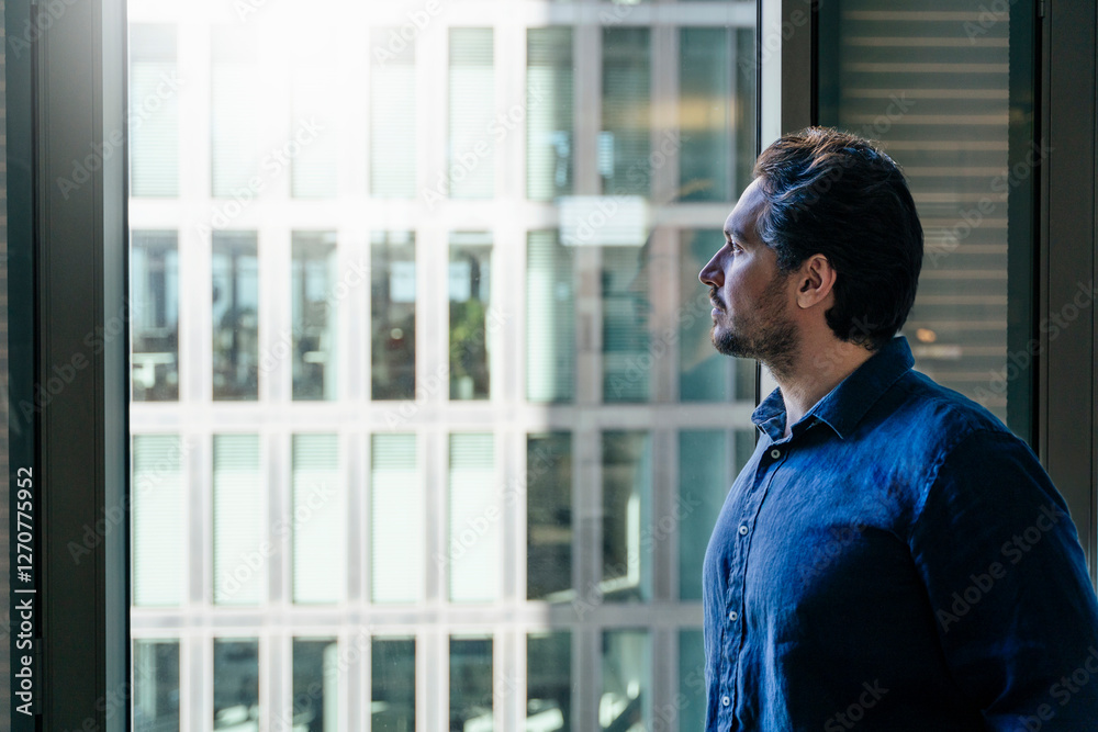 Businessman looking through window in office Businessman looking through window in office