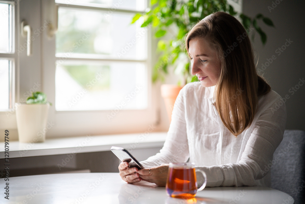 Long haired woman spending leisure time using smart phone at table in home Long haired woman spending leisure time using smart phone at table in home