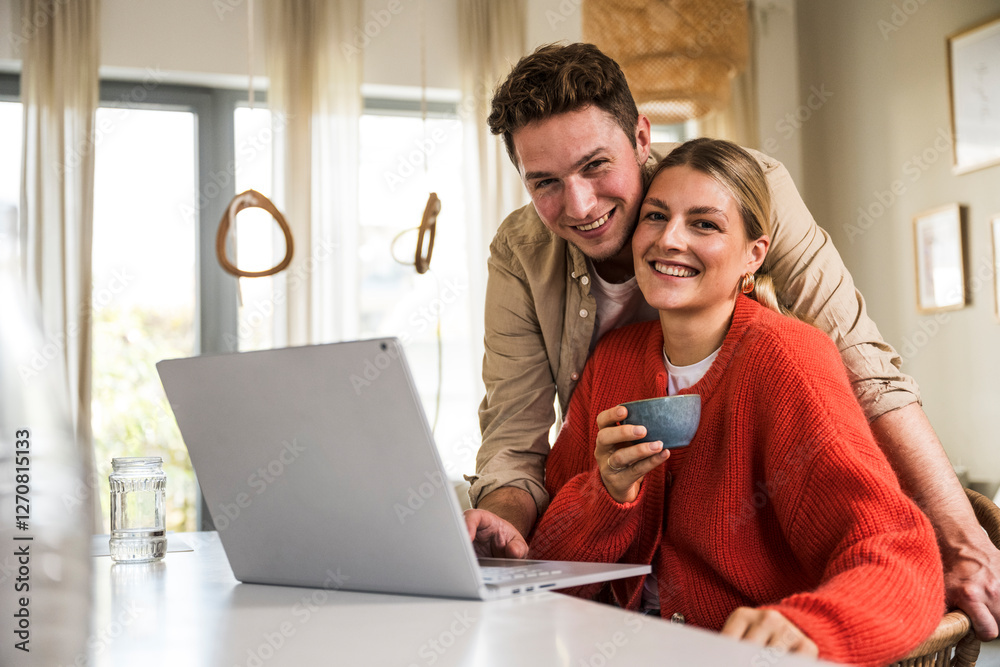 Smiling man and woman sitting at table near laptop in home Smiling man and woman sitting at table near laptop in home