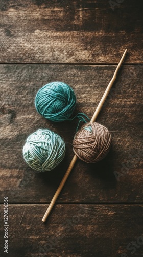 Yarn balls and knitting needles arranged on a rustic wooden surface for creat...