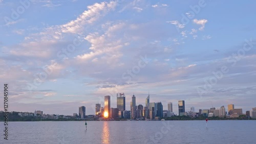 A day in Perth city turns to dusk viewed over the Swan River. Paddle boarder passes. Sun glints off skyscrapers. Time Lapse
