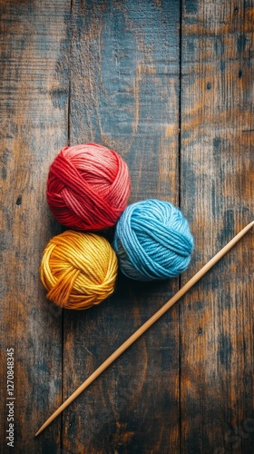 Yarn balls and knitting needles arranged on a rustic wooden surface for creat...