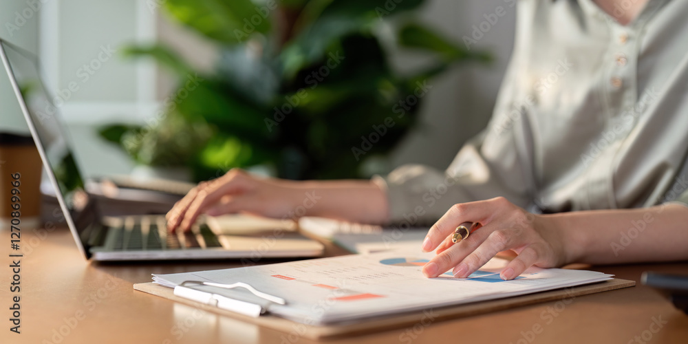 Financial analyst reviewing charts and data on clipboard while using laptop for calculations. Financial analyst reviewing charts and data on clipboard while using laptop for calculations.