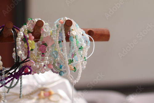Collection of colorful beaded bracelets displayed on a wooden rack. The bracelets are made from various pastel and vibrant beads with a blurred red background adding depth to the image.