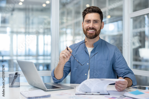 Wallpaper Mural Portrait of successful financier at workplace, man smiling and looking at camera. Businessman behind paperwork with graphs and charts, using laptop. Satisfied accountant investor. Torontodigital.ca