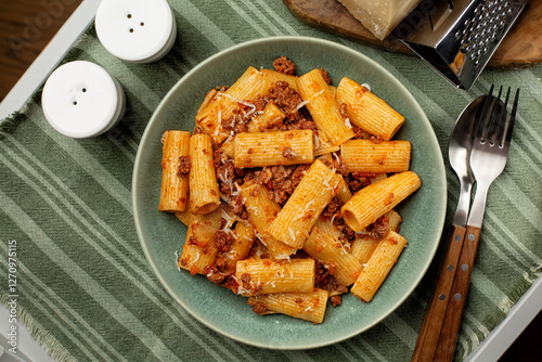 Italian pasta rigatoni with meat bolognese sauce and hard cheese parmesan in a green plate. Top view.