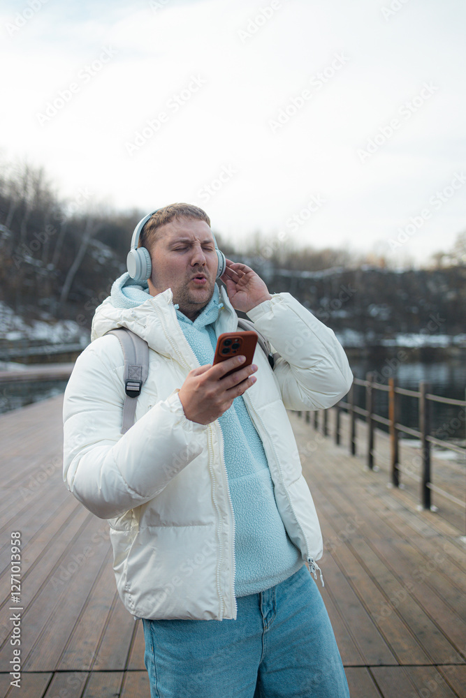 Smiling young man is walking near a lake on the forest, wearing headphones and using a mobile phone. High quality photo Smiling young man is walking near a lake on the forest, wearing headphones and using a mobile phone. High quality photo