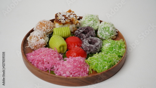 Various market snacks consisting of klepon, awug, jalabria, getuk, putu mayang and cikak are served on a wooden plate lined with banana leaves placed on a white base and background (isolated white). photo