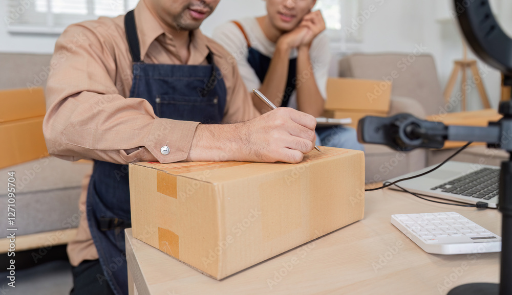 Focused online seller writing shipment details while another looks on, showcasing teamwork and efficiency. Focused online seller writing shipment details while another looks on, showcasing teamwork and efficiency.